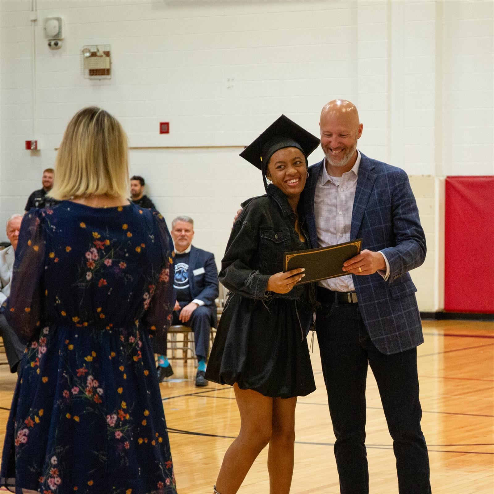 A smiling graduate receives a diploma during a school ceremony, representing our core value of excellence.
